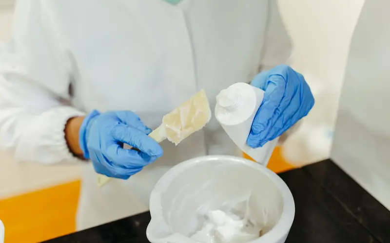 Laboratuvarda eldivenli uzman kozmetik krem karıştırıyor