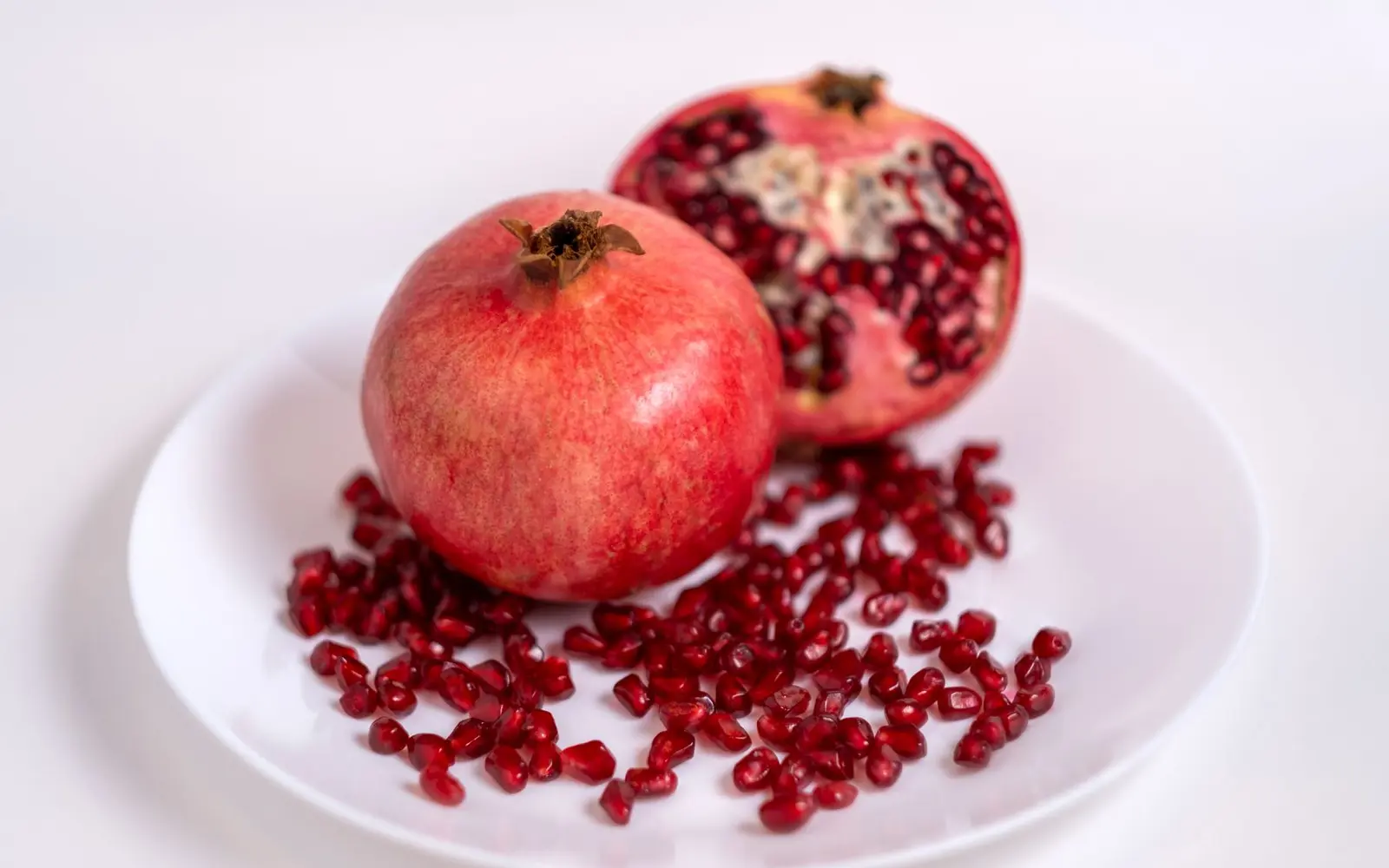 Close-up of fresh and juicy pomegranates on a white plate, highlighting organic red seeds.