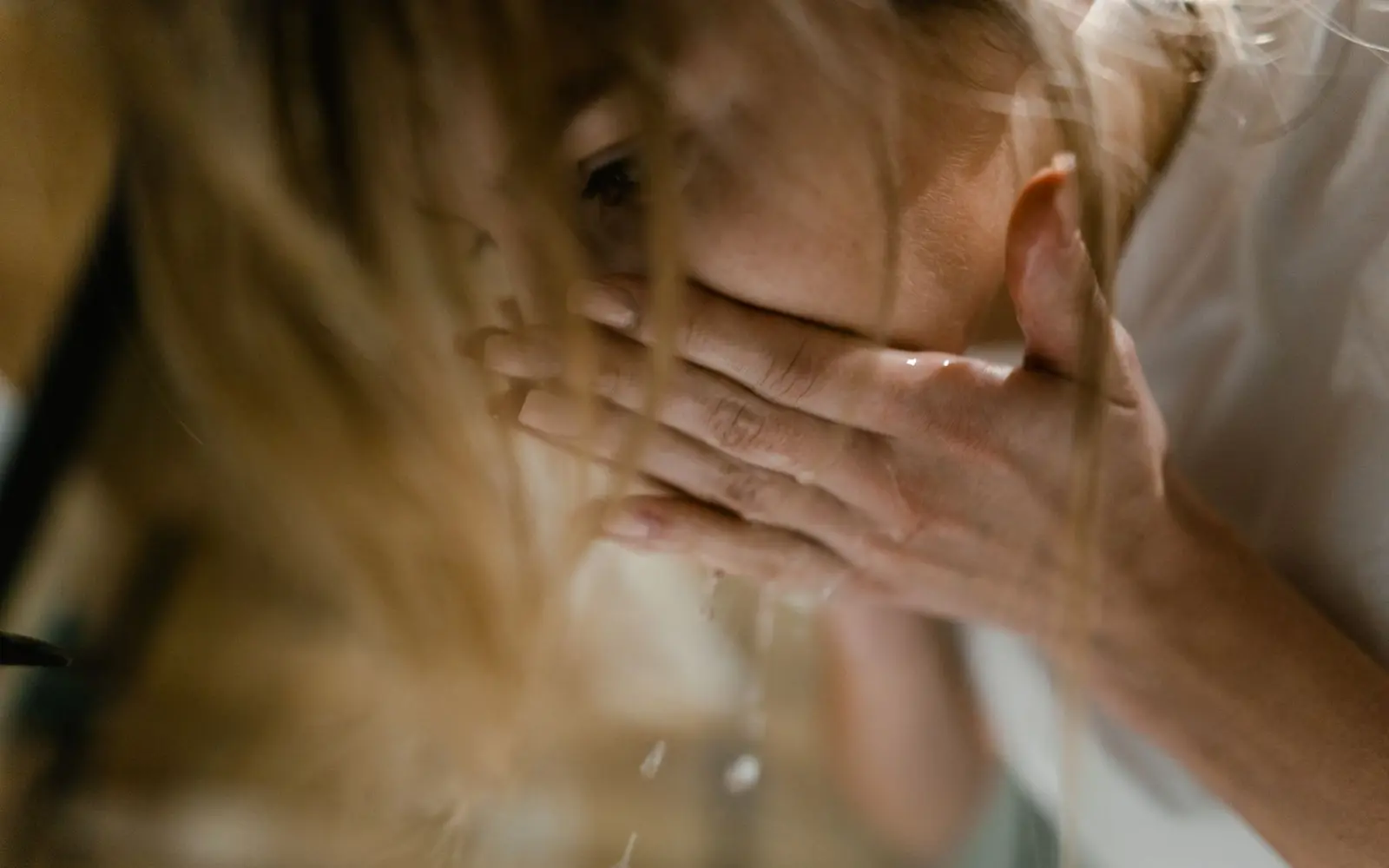 A woman splashes water on her face, emphasizing refreshing skincare routine.