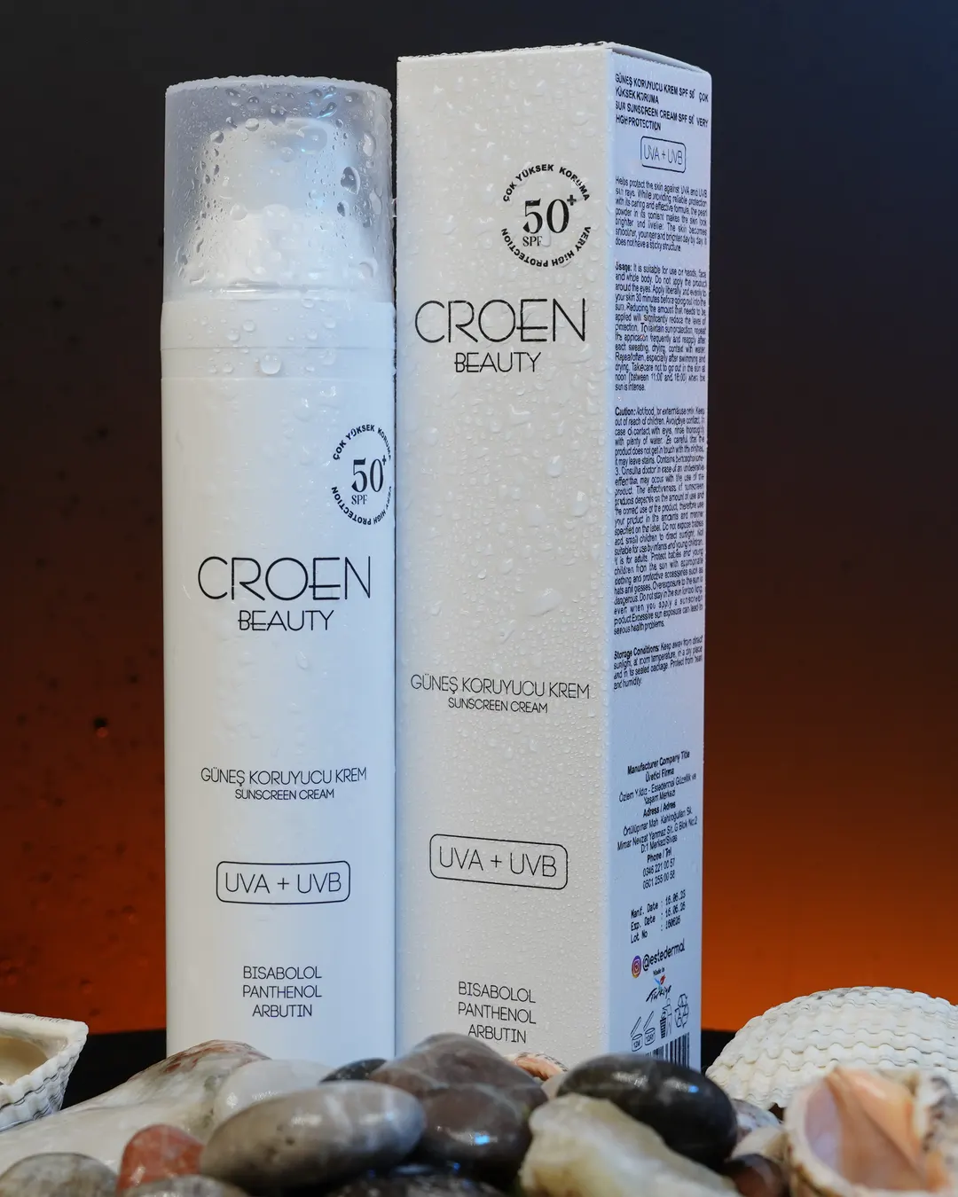 Croen Güneş Koruyucu Krem SPF 50+ şişesi ve kutusu, turuncu ışıkta taşlar üzerinde